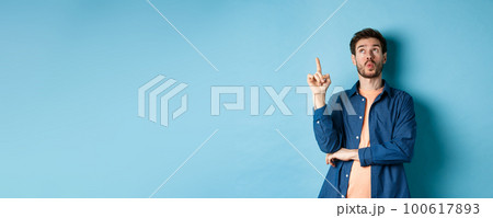 Image of handsome man pitching an idea, raising finger and looking up thinking, standing on blue background 100617893