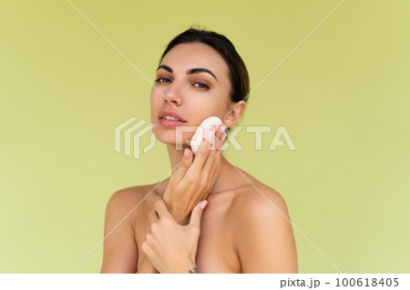 Beauty portrait of young woman with bare shoulders on green background with cosmetic powder puff velour makeup foundation blender sponge applicator 100618405