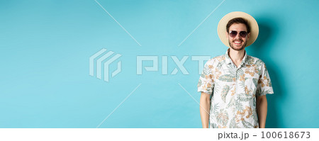 Handsome smiling guy in sunglasses and summer shirt, enjoying vacation on tour, standing on blue background Handsome smiling guy in sunglasses and summer shirt, enjoying vacation on tour, standing on blue background 100618673