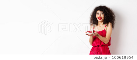 Birthday girl holding cake and making wish, smiling and celebrating, wearing festive red dress, white background Birthday girl holding cake and making wish, smiling and celebrating, wearing festive red dress, white background 100619954