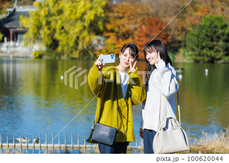 公園の水辺で自撮りする若い女性 100620044