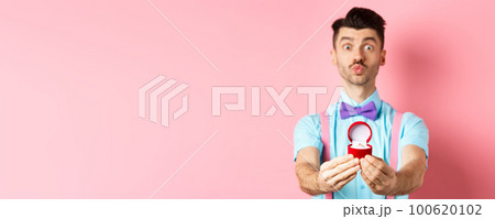 Valentines day. Funny young man pucker lips for kiss and showing engagement ring, making proposal, say marry me to lover, standing over pink background Valentines day. Funny young man pucker lips for kiss and showing engagement ring, making proposal, say marry me to lover, standing over pink background 100620102