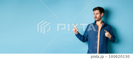 Image of young caucasian man looking and pointing aside, showing advertisement, standing on blue background Image of young caucasian man looking and pointing aside, showing advertisement, standing on blue background 100620130