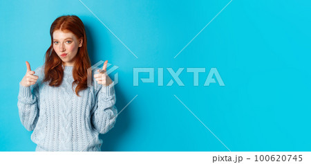 Proud redhead girl pointing fingers at camera, praising and saying congrats, standing over blue background 100620745