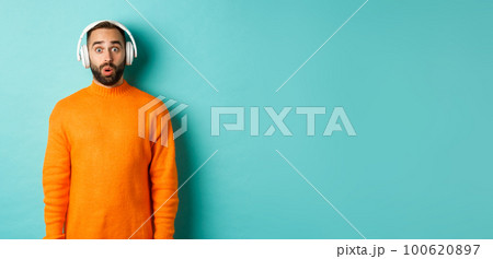 Amazed adult man listening music in headphones, looking at camera impressed with sound, standing over turquoise background Amazed adult man listening music in headphones, looking at camera impressed with sound, standing over turquoise background 100620897
