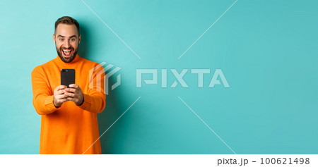 Image of man reading awesome message on mobile phone, looking at smartphone screen with amazement, standing over light blue background Image of man reading awesome message on mobile phone, looking at smartphone screen with amazement, standing over light blue background 100621498
