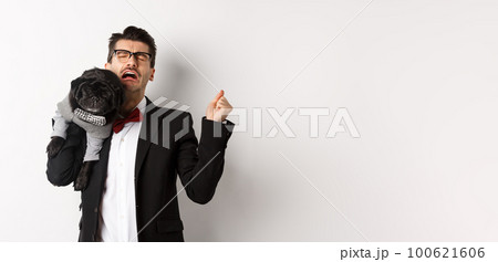 Sad man in suit, holding cute small dog on shoulder and crying with disappointed face, standing distressed over white background 100621606