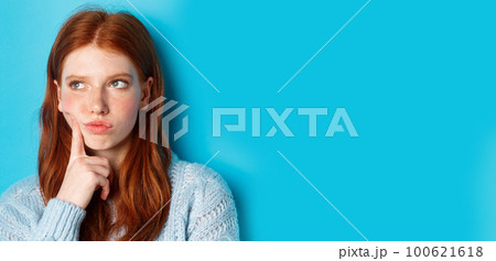Headshot of troubled teenage girl thinking, looking bothered and frowning, standing against blue background 100621618