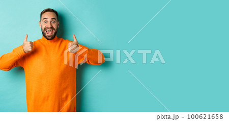 Amazed man showing thumbs-up, approve and praise something awesome, cool thing, standing over light blue background Amazed man showing thumbs-up, approve and praise something awesome, cool thing, standing over light blue background 100621658