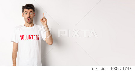 Handsome young man in volunteer t-shirt having an idea, raising finger and saying suggestion, pointing up, standing over white background 100621747
