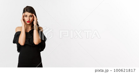 Fashion and beauty. Young modern woman in glamour dress, jewelry and makeup, touching head and looking exhausted, feeling dizzy, standing over white background Fashion and beauty. Young modern woman in glamour dress, jewelry and makeup, touching head and looking exhausted, feeling dizzy, standing over white background 100621817