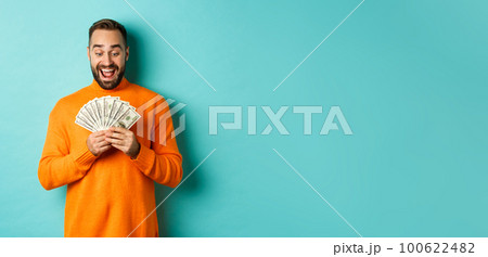 Image of man looking happy at money, smiling amazed, standing over light blue background Image of man looking happy at money, smiling amazed, standing over light blue background 100622482