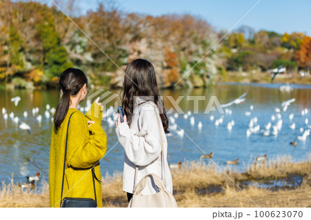 公園の水辺で友達と過ごす若い女性 100623070