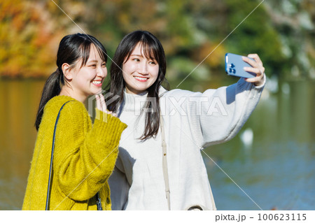 公園の水辺で自撮りする若い女性 100623115