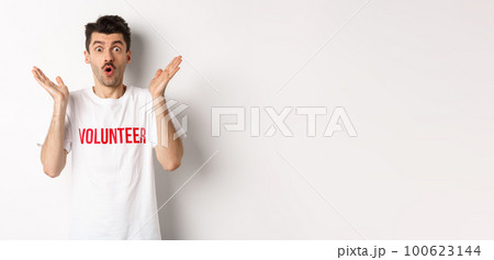 Amazed male volunteer in white t-shirt hear great news, clap hands and staring at camera surprised, posing over studio background 100623144