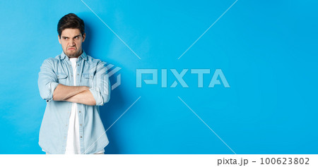 Angry guy cross arms on chest and looking away with insulted expression, standing offended against blue background Angry guy cross arms on chest and looking away with insulted expression, standing offended against blue background 100623802