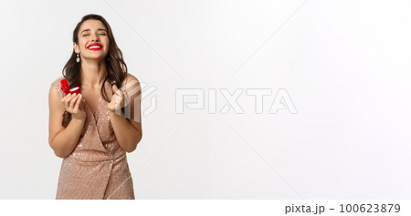 Satisfied and happy woman holding engagement ring and red small box, receive marriage proposal on new year eve, wearing elegant dress, smiling delighted, white background Satisfied and happy woman holding engagement ring and red small box, receive marriage proposal on new year eve, wearing elegant dress, smiling delighted, white background 100623879