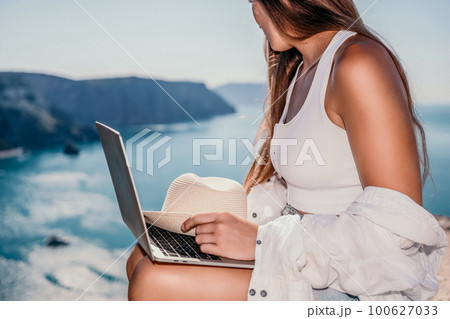 Woman sea laptop. Business woman in yellow hat freelancer with laptop working over blue sea beach. Girl relieves stress from work. Freelance, digital nomad, travel and holidays concept 100627033
