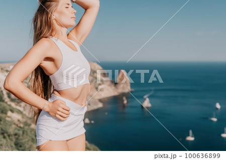 Woman summer travel sea. Happy tourist in hat enjoy taking picture outdoors for memories. Woman traveler posing on the beach at sea surrounded by volcanic mountains, sharing travel adventure journey 100636899
