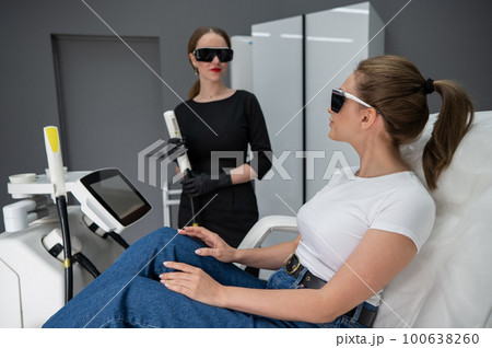 A woman on a couch in goggles undergoing a photorejuvenation procedure. Cosmetologist with a patient. A woman on a couch in goggles undergoing a photorejuvenation procedure. Cosmetologist with a patient. 100638260