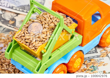 Close-up of twenty cent euro coin in the body of a toy truck that transports grain on a background of dollar bills 100642976