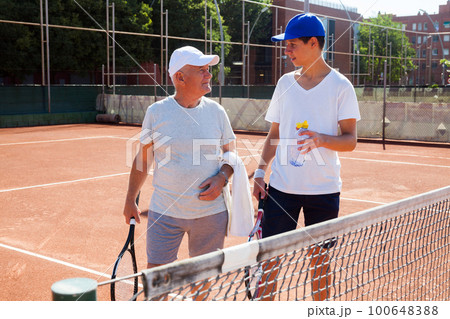 grandfather and grandson talking on court playing tennis grandfather and grandson talking on court playing tennis 100648388