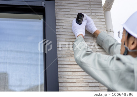 一戸建ての壁に防犯カメラを設置している作業員の男性 一戸建ての壁に防犯カメラを設置している作業員の男性 100648596