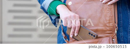 Young woman putting modern smartphone in bag Young woman putting modern smartphone in bag 100650515