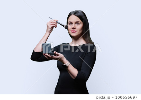 Young woman holding powder and using makeup brush, on white background 100656697