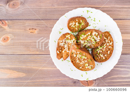 Fresh rye garlic croutons with dill on a plate on a wooden table. Top view. Copy space Fresh rye garlic croutons with dill on a plate on a wooden table. Top view. Copy space 100660096