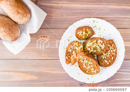 Fresh rye garlic croutons with dill on a plate and buns in a basket on a wooden table. Top view. Copy space Fresh rye garlic croutons with dill on a plate and buns in a basket on a wooden table. Top view. Copy space 100660097