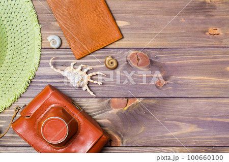 Camera in a case, passport, hat and seashells on a wooden background. Retro style. Place for the inscription. Vacation concept. 100660100