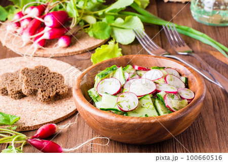 Lenten spring vegetable salad from cucumber, radish, greens and oil in a wooden plate 100660516