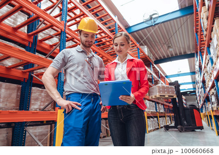 Manager and worker in high bay warehouse discussing business 100660668