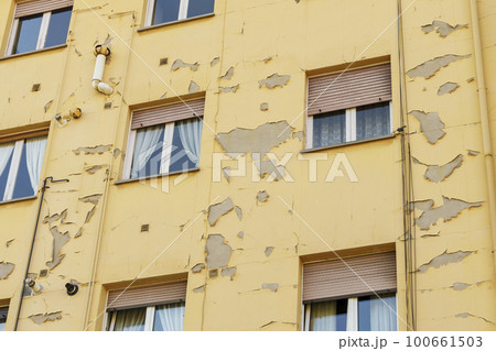Damaged peeling paint on the wall of a residential building on a city street 100661503