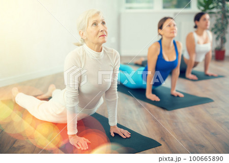 Diligent women practicing cobra pose of yoga in light fitness room 100665890
