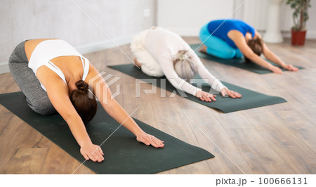 Young female yoga instructor showing others upward facing dog pose in wellness center 100666131