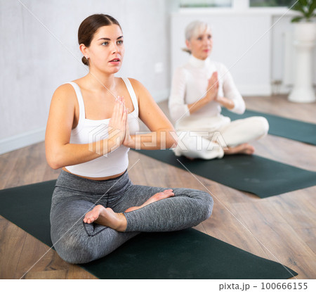 Diligent women practicing lotus pose of yoga in light fitness room 100666155