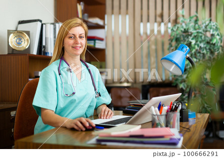 Positive woman doctor working in cabinet on laptop 100666291