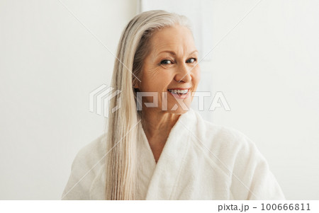Cheerful female with gray hair in a bathrobe looking at her reflection	 100666811