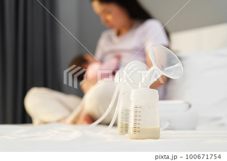 the breast milk are in the bottles of electric breast pumping set on bed with mother breastfeeding newborm baby background the breast milk are in the bottles of electric breast pumping set on bed with mother breastfeeding newborm baby background 100671754