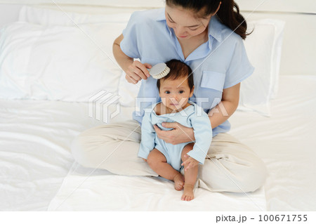 mother combing her newborn baby hair on bed mother combing her newborn baby hair on bed 100671755
