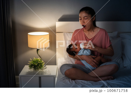 sleepy mother yawning and feeding milk bottle to newborn baby on bed at night sleepy mother yawning and feeding milk bottle to newborn baby on bed at night 100671758