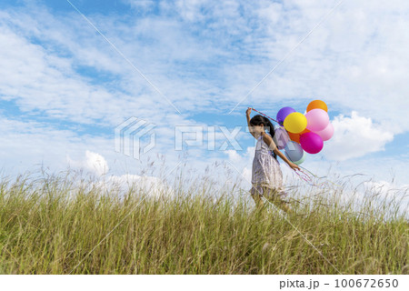Cheerful cute girl holding balloons running on green meadow white cloud and blue sky with happiness. Hands holding vibrant air balloons play on birthday party happy times summer on sunlight outdoor Cheerful cute girl holding balloons running on green meadow white cloud and blue sky with happiness. Hands holding vibrant air balloons play on birthday party happy times summer on sunlight outdoor 100672650