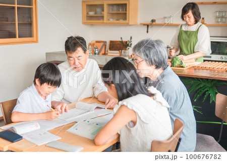 家のダイニングで孫の宿題を教える高齢者夫婦と小学生の子供 100676782