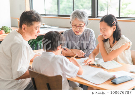 家のダイニングで孫の宿題を教える高齢者夫婦と小学生の子供 100676787