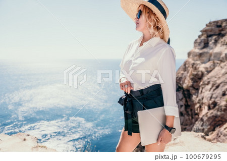 Woman sea laptop. Business woman in yellow hat freelancer with laptop working over blue sea beach. Girl relieves stress from work. Freelance, digital nomad, travel and holidays concept 100679295