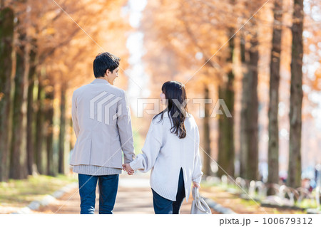 手をつないで並木道を歩く若いカップル 手をつないで並木道を歩く若いカップル 100679312