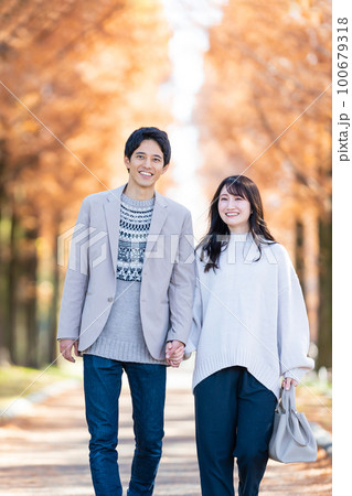 手をつないで並木道を歩く若いカップル 手をつないで並木道を歩く若いカップル 100679318