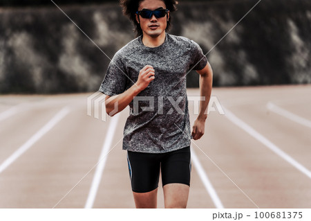 陸上競技のトラックの直線を走るサングラスをかけた男性ランナー 100681375